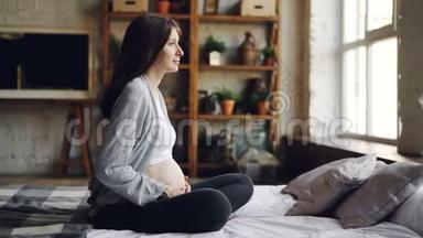 可<strong>爱</strong>的<strong>孕</strong>妇正坐在床上望着窗外，抚摸着她的腹部，感觉婴儿在里面